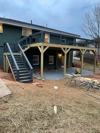 Elevated deck under construction with wooden post frame attached to a dark-sided residential home
