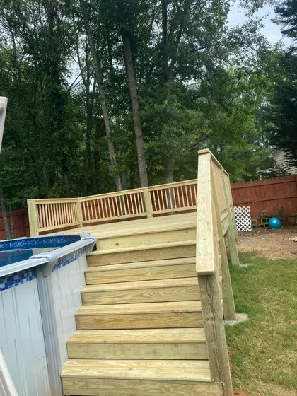 Wooden deck platform and stairs leading to an above-ground pool in a fenced backyard