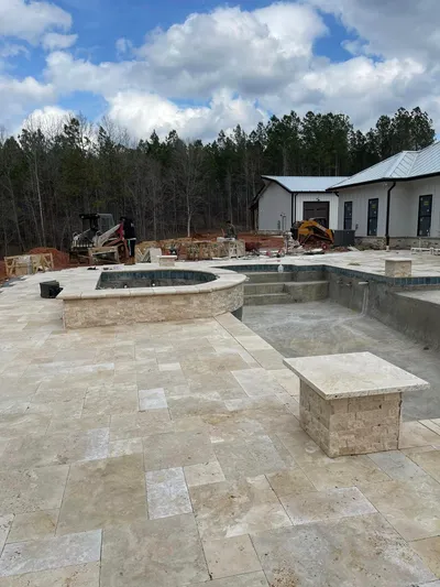 Large travertine patio with circular spa surround and outdoor kitchen under construction at new home