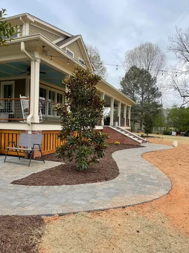 Curved paver walkway with fresh mulch bed around a magnolia tree in front of a craftsman-style home